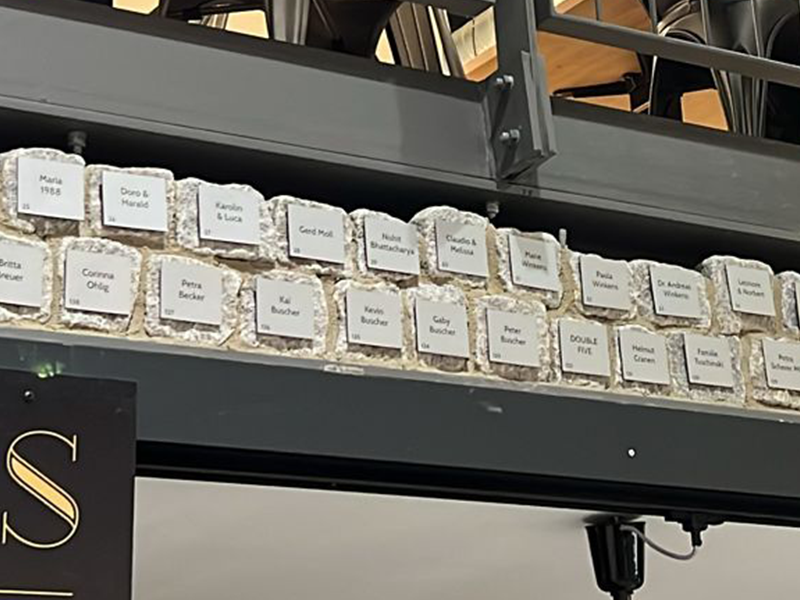 Bei gutem Wetter steht eine große Gruppe von Menschen versammelt um aufgebaute Zelte und Pavillons auf dem neu eröffneten Kapuzinerplatz, vor dem Haus Zoar.